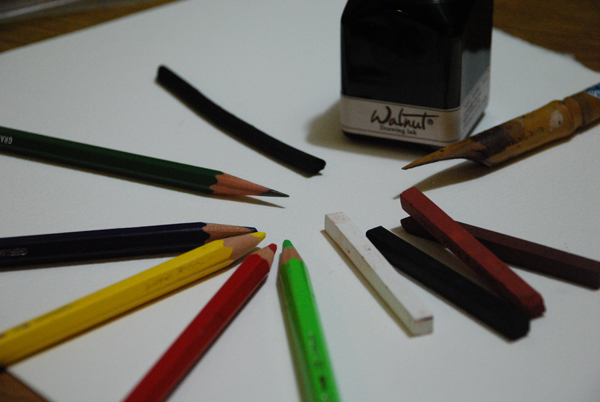 A bottle of walnut ink and a bamboo pen, four colors of Conté crayons (bistre, sanguine, black, and white), four colors of colored pencils, a graphite pencil, and a piece of vine charcoal.